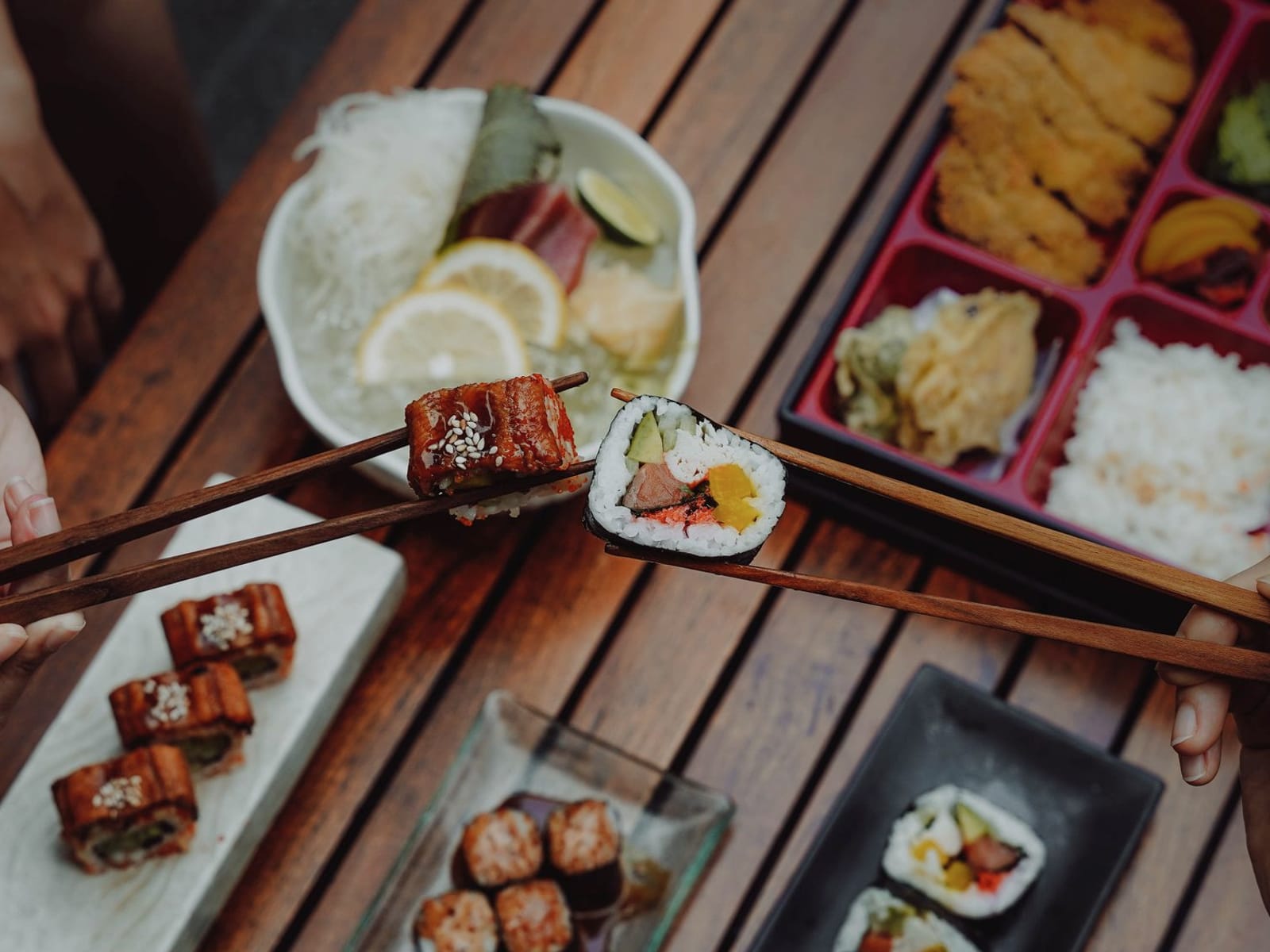 Mãos compartilhando sushi com hashi sobre mesa de madeira